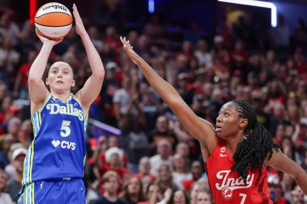 Paige Bueckers, left, of the Dallas Wings rises to shoot with a basketball cupped in her right hand as Aliyah Boston of the Indiana Fever reaches out to defend with her right arm.
